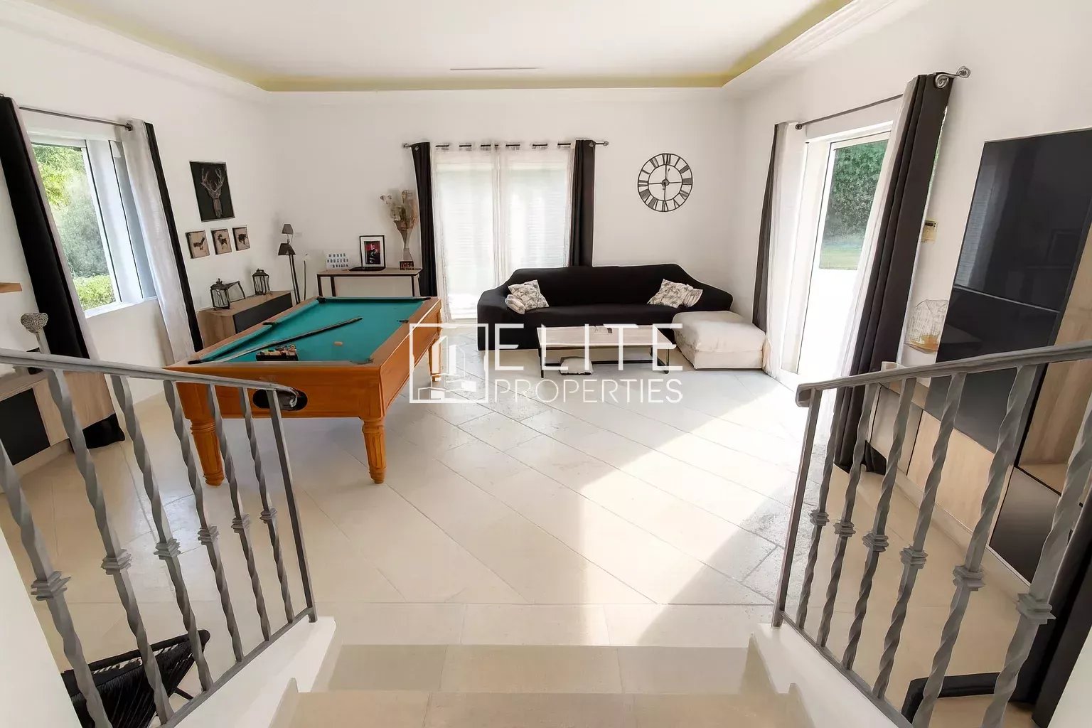 Interior of a villa with a pool table, a sofa and windows overlooking the outside.