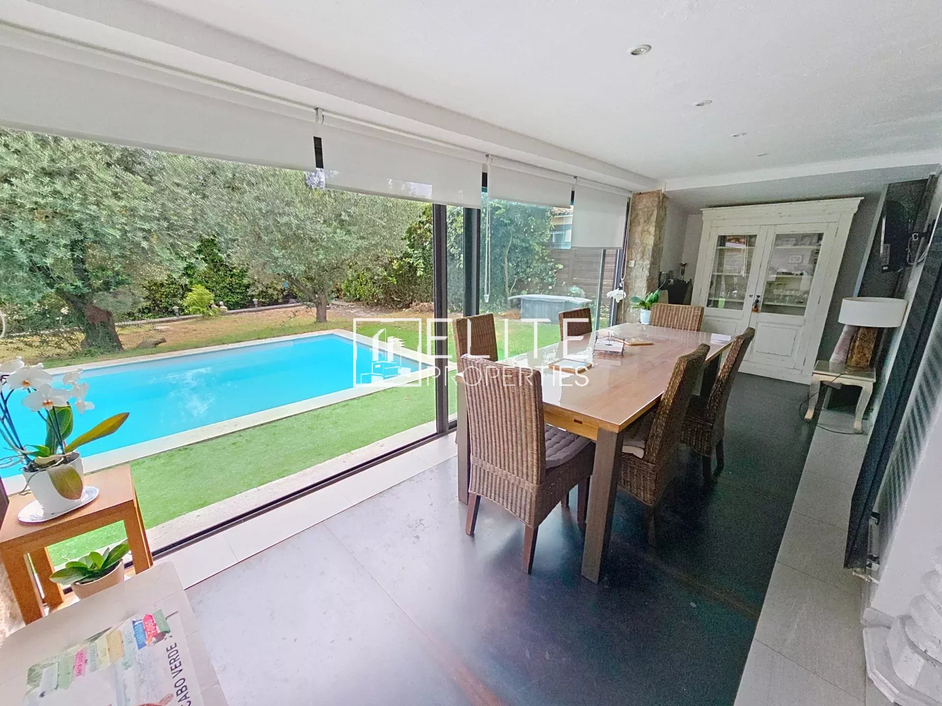 Intérieur d'une maison avec vue sur une piscine, mobilier moderne, et jardin verdoyant.