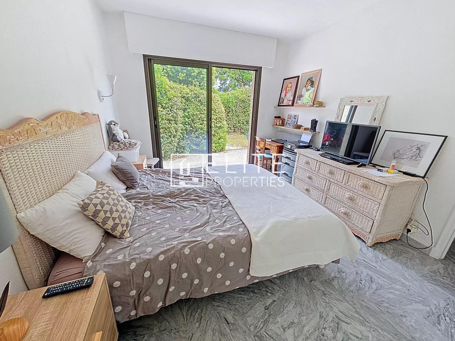 Chambre d'une maison à Mougins avec lit, meubles en osier et fenêtre donnant sur un jardin.