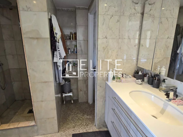 Salle de bain moderne avec douche et lavabo, murs en marbre, produits de beauté sur le plan de travail.