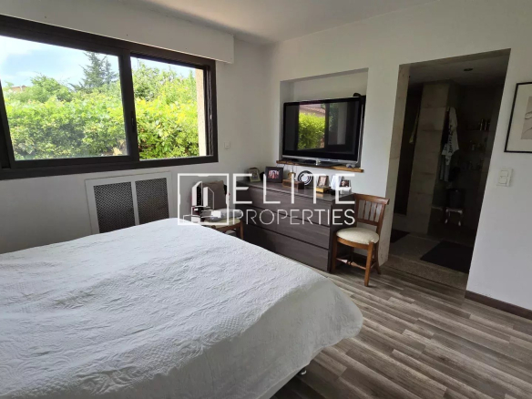 Chambre d'une maison à Mougins avec lit, bureau et fenêtres donnant sur un jardin.