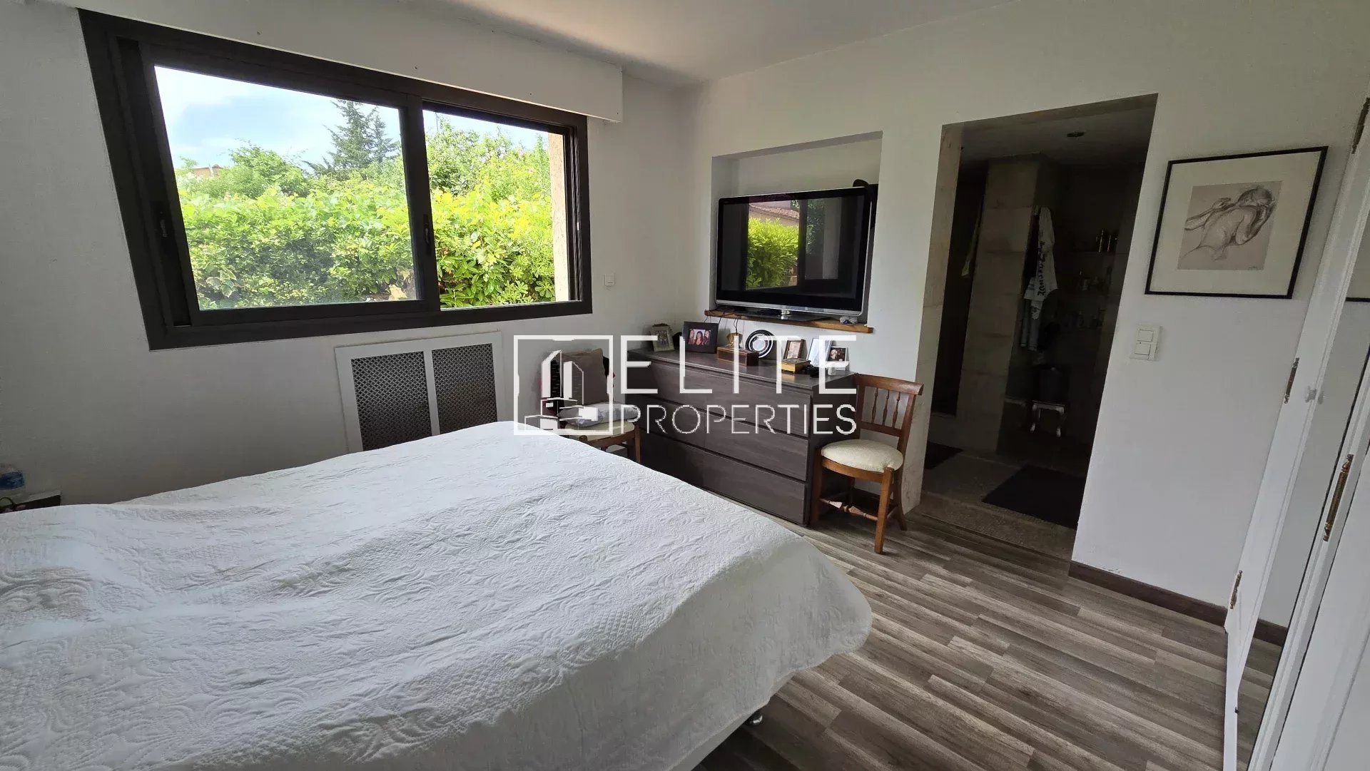 Chambre d'une maison à Mougins avec lit, bureau et fenêtres donnant sur un jardin.