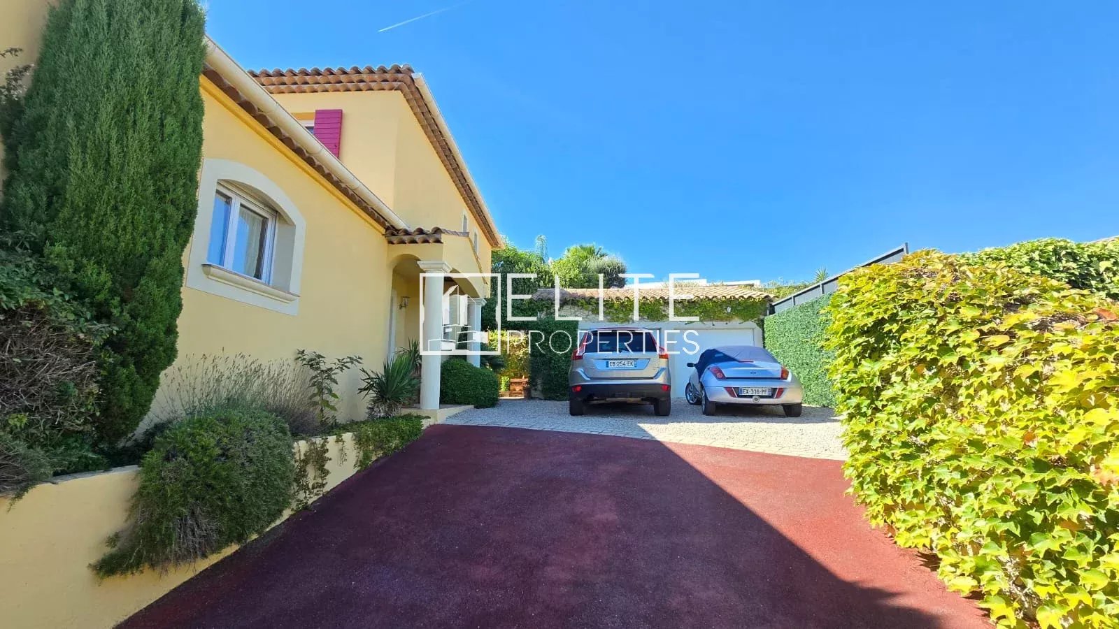 Maison à Tanneron avec jardin et voitures Entrée d'une maison à Tanneron avec deux voitures garées et un jardin verdoyant.