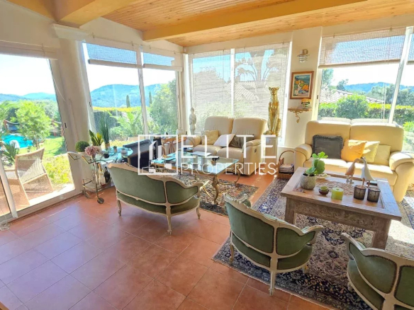 Intérieur d'une maison avec salon lumineux et vue sur la piscine et le jardin.