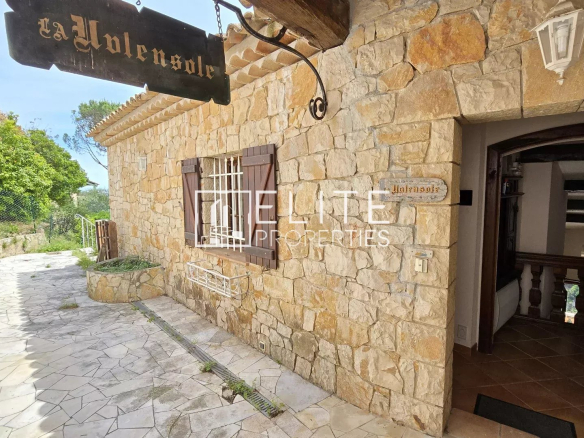 Entrée d'une maison en pierre avec un panneau en bois, entourée de verdure à Mandelieu-la-Napoule.