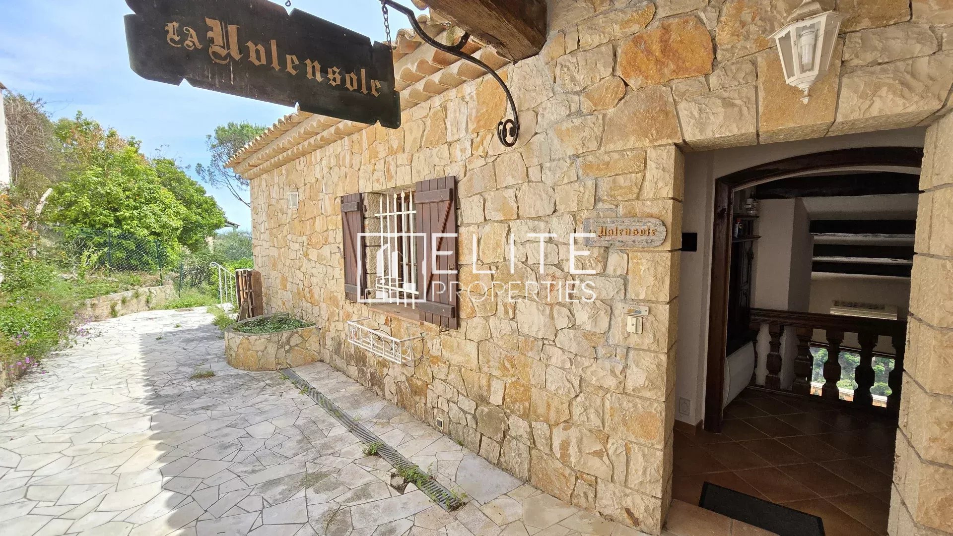 Entrée de maison à Mandelieu-la-Napoule Entrée d'une maison en pierre avec un panneau en bois, entourée de verdure à Mandelieu-la-Napoule.
