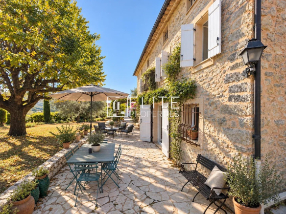 Terrasse d'une bergerie en pierres à Saint-Antoine, Grasse, avec mobilier de jardin et parasol.
