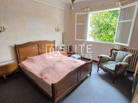 Chambre d'un appartement avec un lit en bois et un fauteuil, fenêtres ouvertes sur l'extérieur.