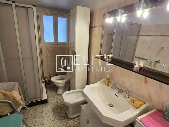 Salle de bain d'un appartement avec lavabo, toilettes et douche, décorée de carrelage beige.