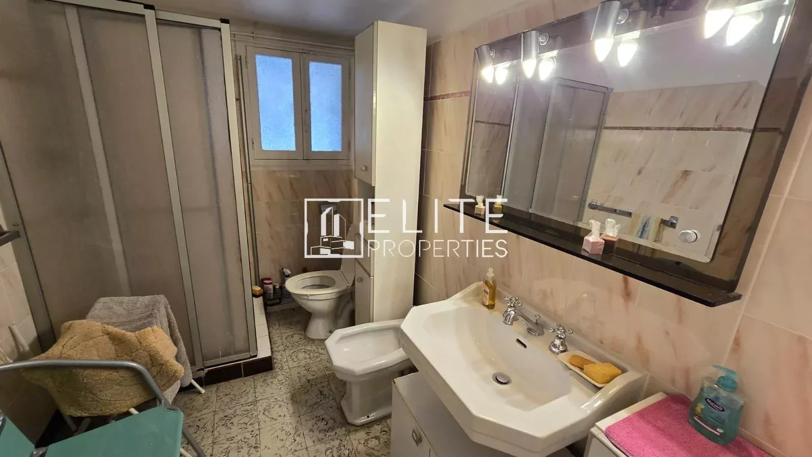 Salle de bain d’un appartement à Juan-les-Pins Salle de bain d'un appartement avec lavabo, toilettes et douche, décorée de carrelage beige.