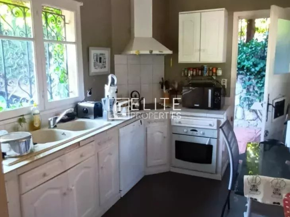 Cuisine d'une maison de plain-pied à Mougins, avec meubles clairs et fenêtre donnant sur l'extérieur.