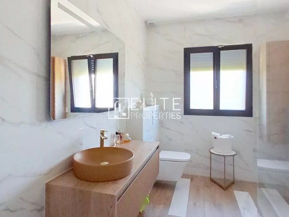 Modern bathroom with wooden furniture and mirror, marble walls, windows with blinds.