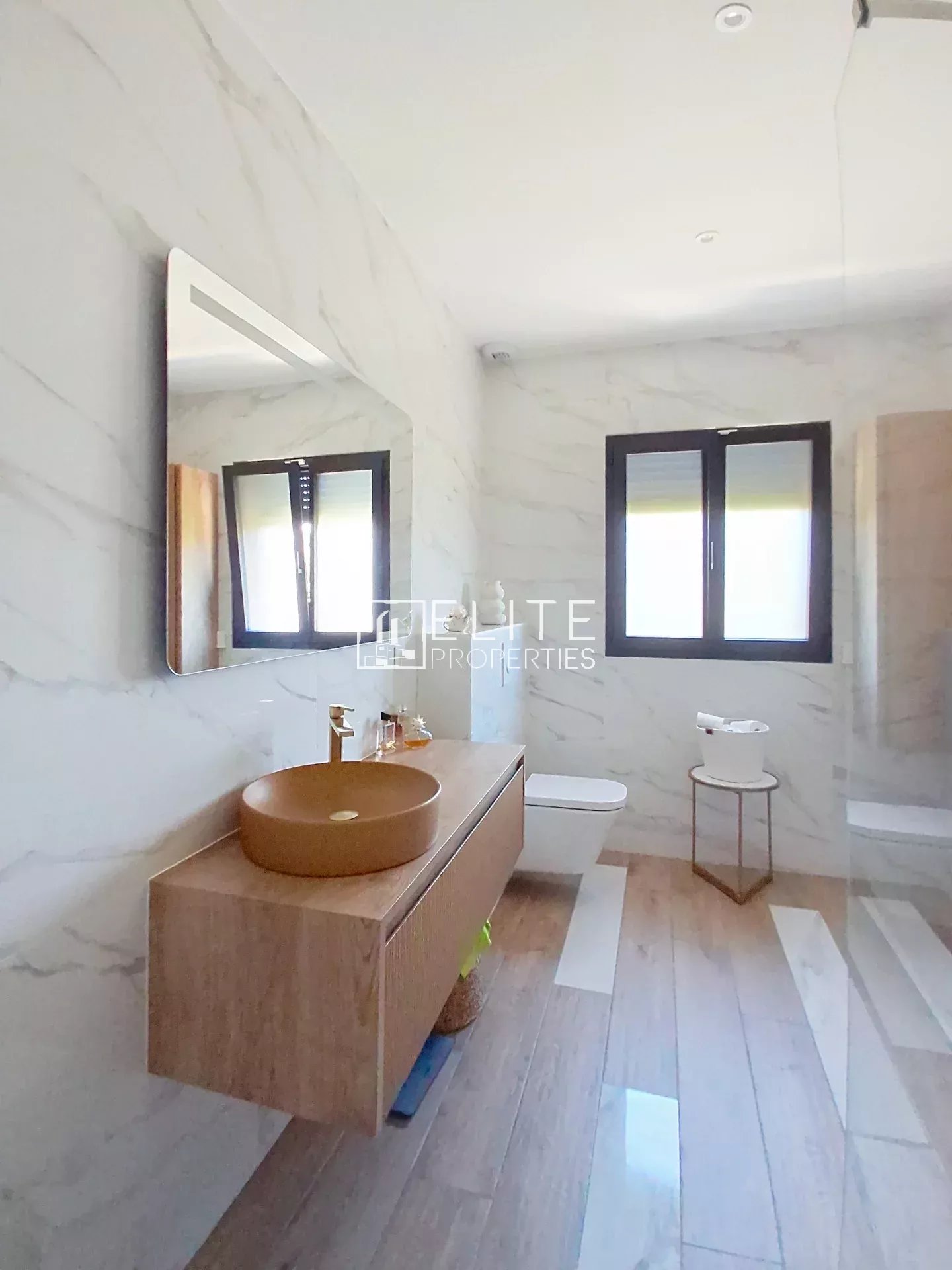 Elegant bathroom in a renovated villa Modern bathroom with wooden furniture and mirror, marble walls, windows with blinds.