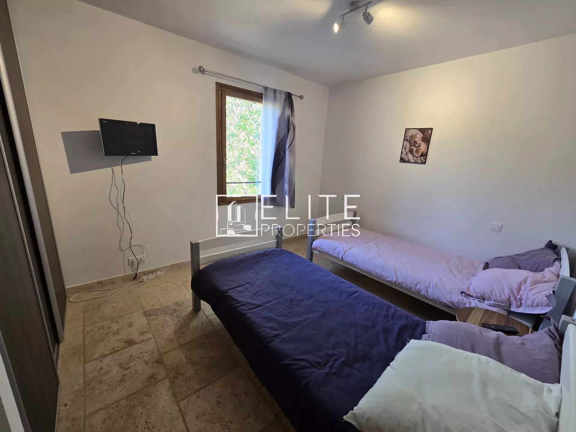 Chambre avec deux lits simples et télévision murale dans une maison à Saint-Vallier-de-Thiey.