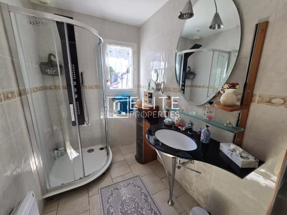Salle de bain moderne avec douche et lavabo, fenêtre laissant entrer la lumière.