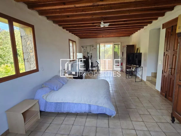 Intérieur d'une maison en pierre avec lit, télévision et fenêtres donnant sur l'extérieur.