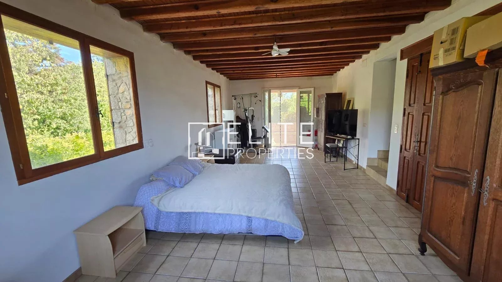 Intérieur d’une maison en pierre à Mouans-Sartoux Intérieur d'une maison en pierre avec lit, télévision et fenêtres donnant sur l'extérieur.