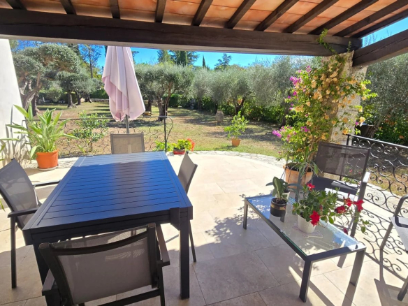Terrasse d'une maison avec table et chaises, vue sur un jardin avec oliviers.