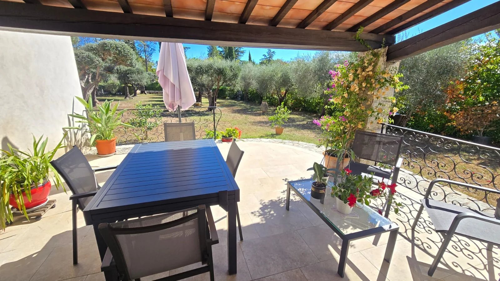Terrasse avec vue sur le jardin Terrasse d'une maison avec table et chaises, vue sur un jardin avec oliviers.