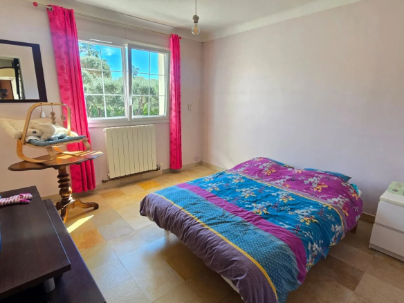 Chambre d'une maison avec lit, meuble TV et fenêtre laissant entrer la lumière.