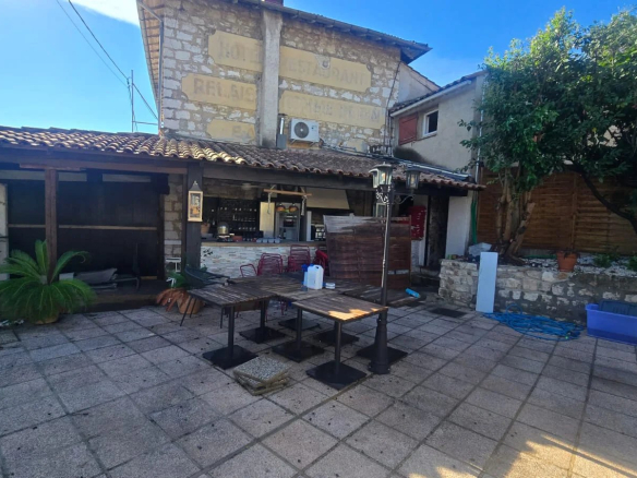Terrasse d'un restaurant avec tables en bois et bar, entourée de murs en pierre à Roquefort-les-Pins.