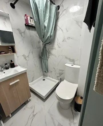 Salle de bain moderne avec douche, lavabo et toilettes, carrelage en marbre.
