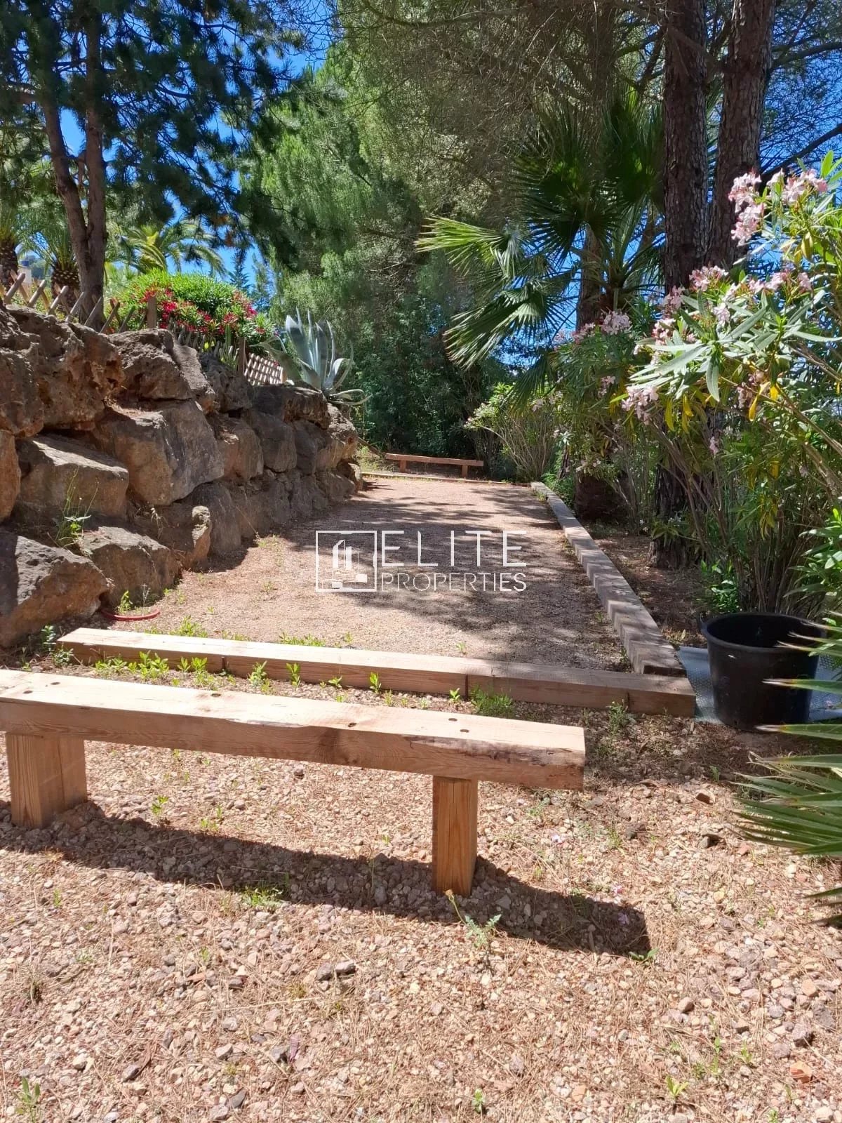 Allée en pierre avec bancs en bois dans un jardin arboré aux Adrets-de-l'Estérel.
