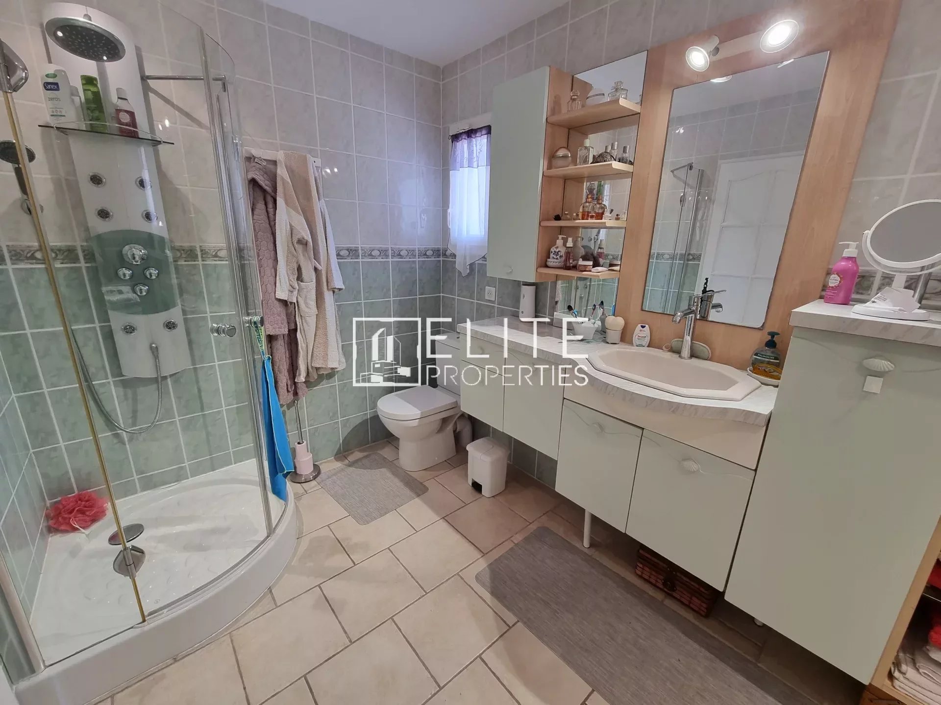 Salle de bain moderne avec douche, lavabo et toilettes, carrelage clair.