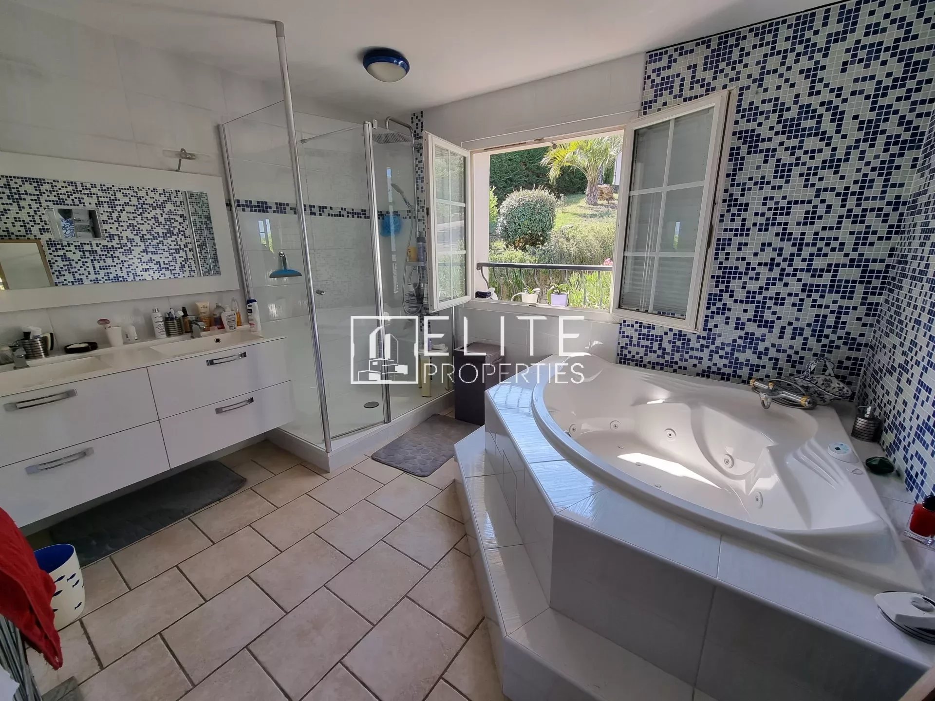 Salle de bain moderne avec baignoire et douche, carrelage clair et mosaïque bleue.