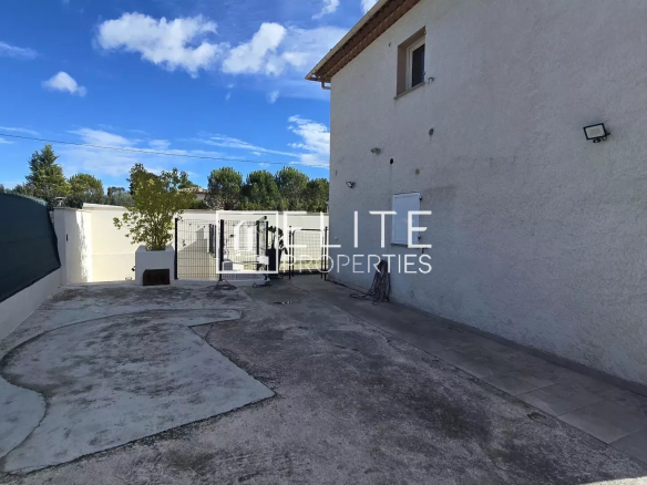 Vue extérieure d'une maison rénovée à Grasse, avec un terrain dégagé.
