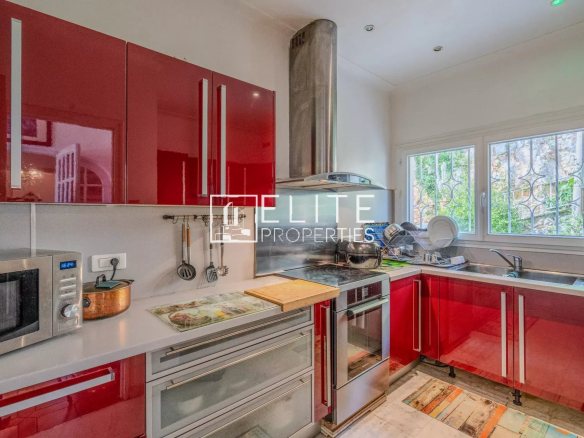 Cuisine moderne avec des meubles rouges et des équipements en inox, lumineuse avec une fenêtre.