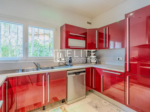 Cuisine moderne avec meubles rouges et équipements en inox, lumineuse grâce à une fenêtre.