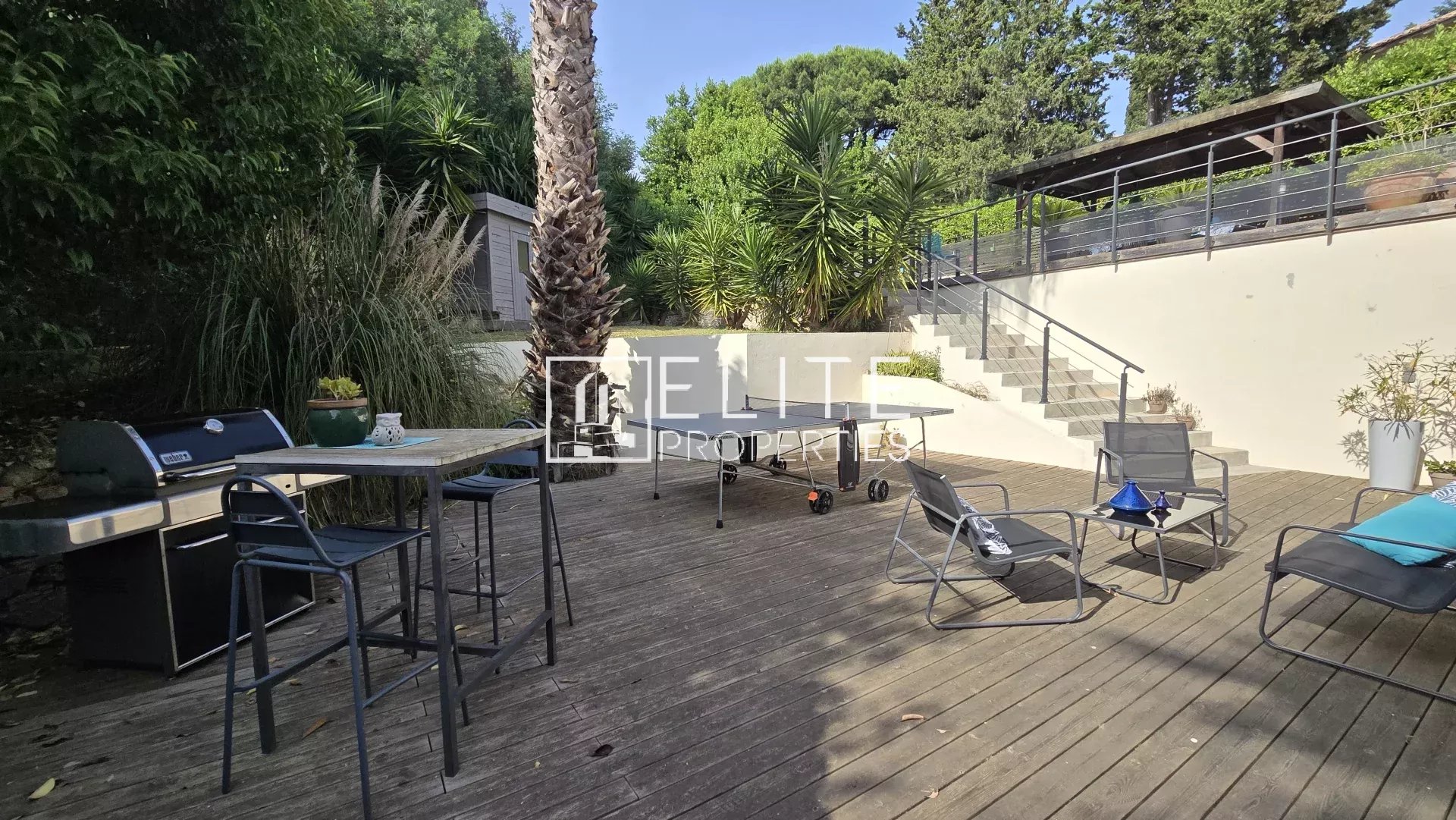 House terrace with unobstructed view Wooden terrace with garden furniture and barbecue, surrounded by greenery.