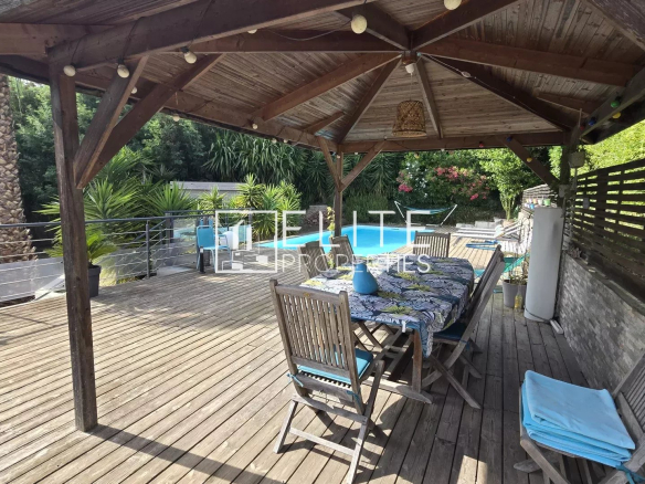 Wooden terrace with garden furniture and swimming pool, surrounded by greenery.