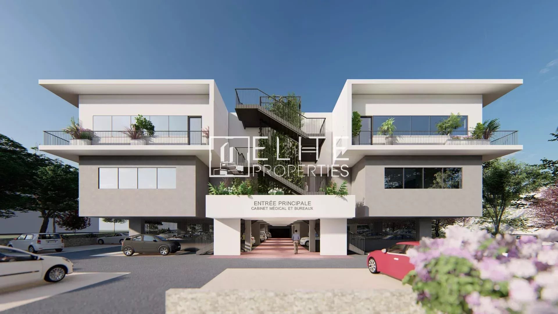Immeuble commercial moderne avec stationnement à Grasse, façade blanche et verdure.