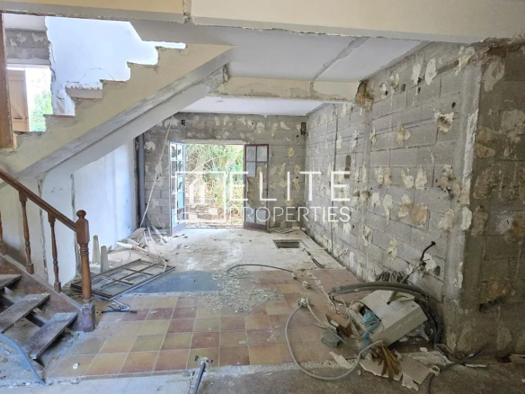 Intérieur d'une maison individuelle abandonnée à rénover, avec des murs en béton et un escalier en bois.