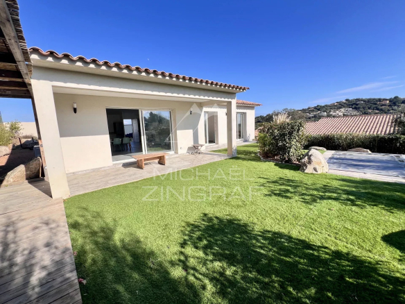 Single-story house with beige exterior and terracotta roof, sliding glass doors open to a patio overlooking a green lawn.