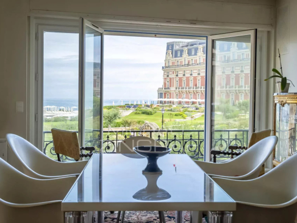 Vue depuis un appartement lumineux avec une table et des chaises, donnant sur l'océan et l'hôtel du Palais à Biarritz.