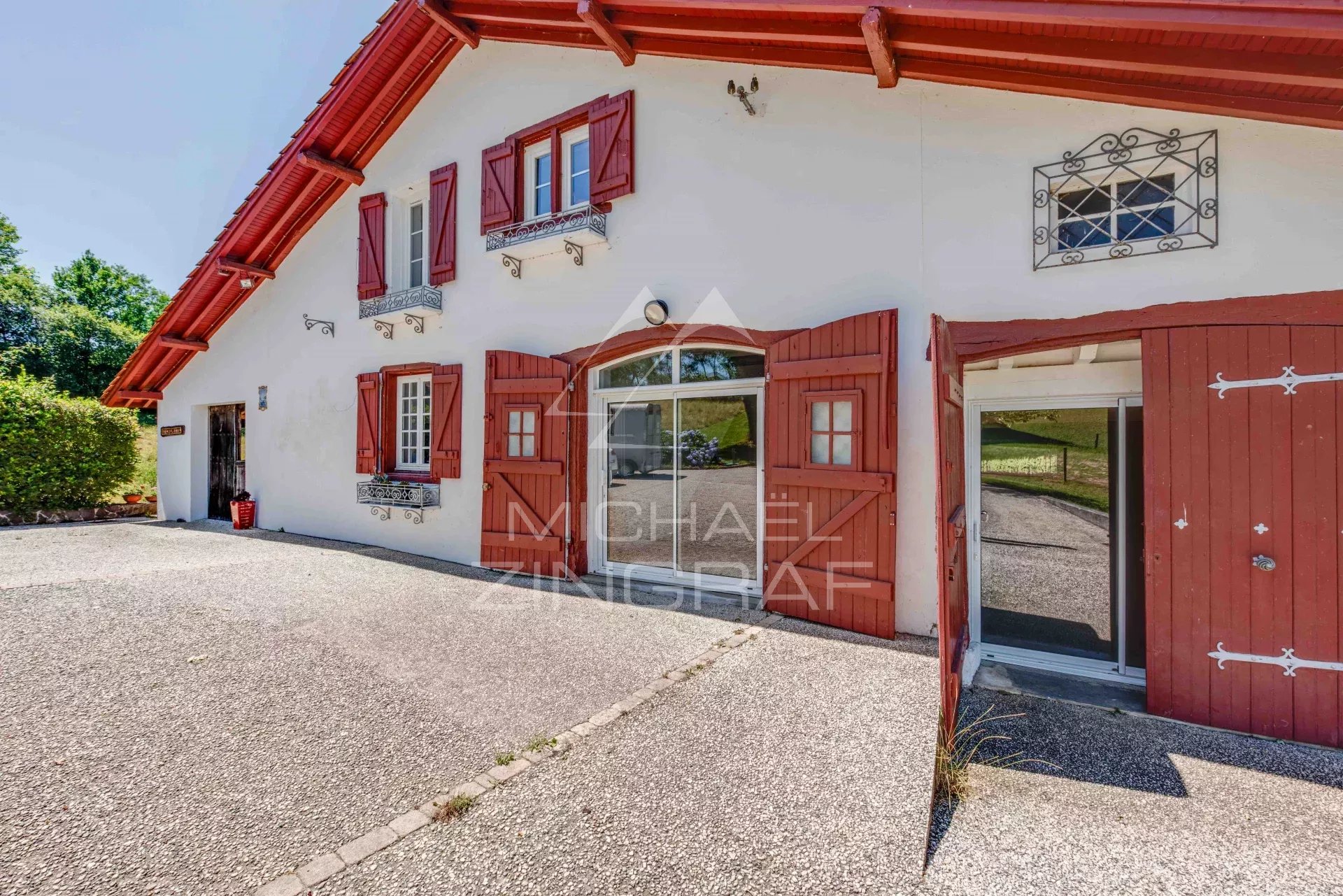 Renovated old farmhouse with red and white facade, surrounded by greenery.