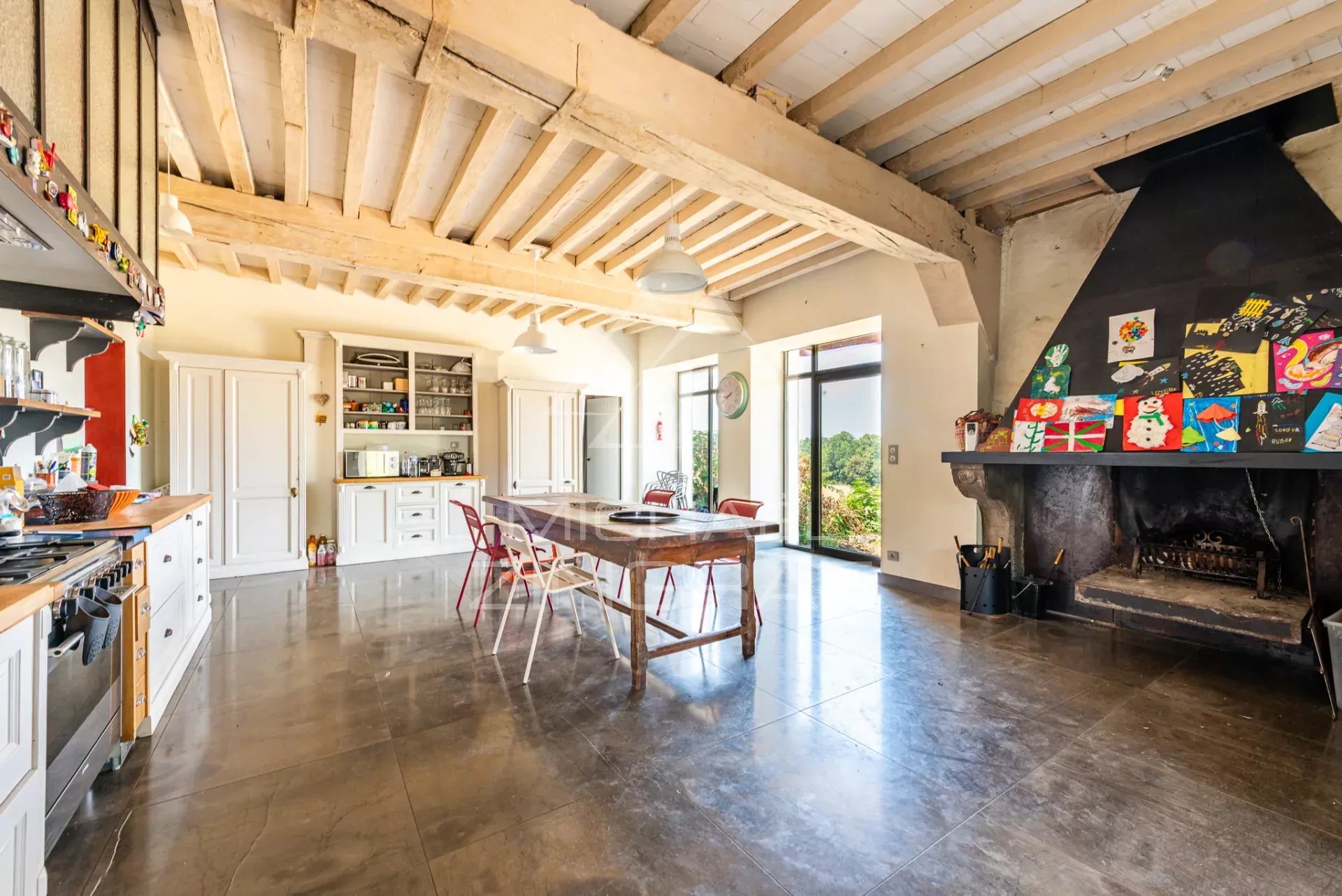 Cuisine spacieuse avec cheminée Intérieur d'une cuisine spacieuse avec table en bois, cheminée et grandes fenêtres donnant sur le jardin.
