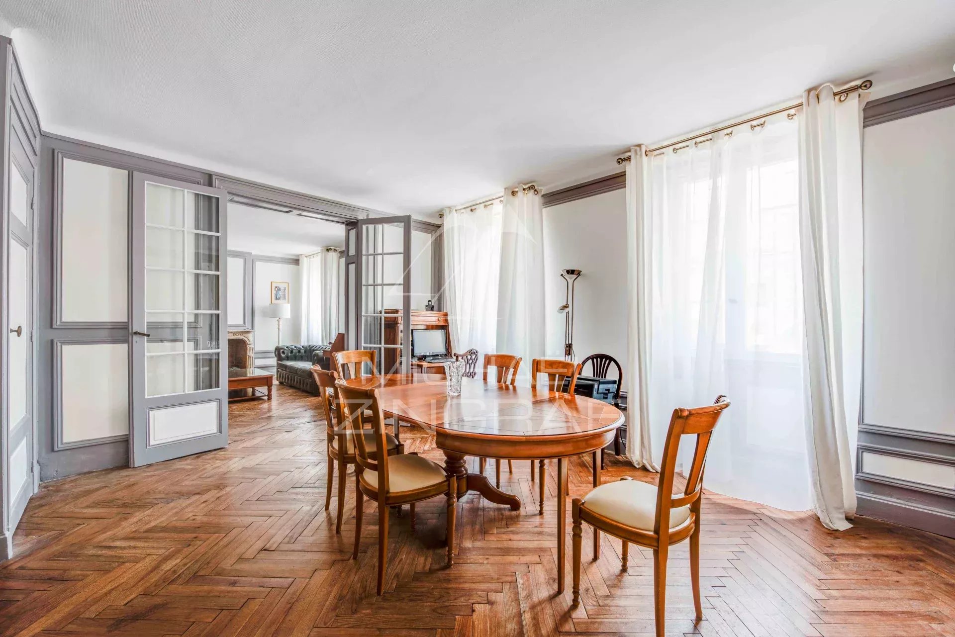 Intérieur d'un appartement spacieux avec un salon et une salle à manger, parquet en bois et lumière naturelle.