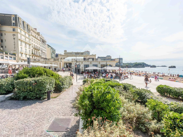 Vue de la plage et des restaurants à Biarritz, avec des gens se détendant sur le sable.