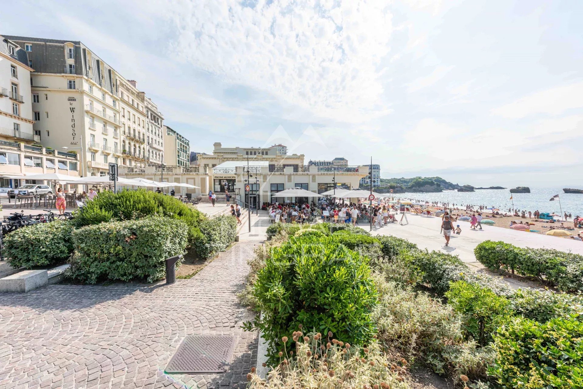 Vue de la plage et des restaurants à Biarritz, avec des gens se détendant sur le sable.