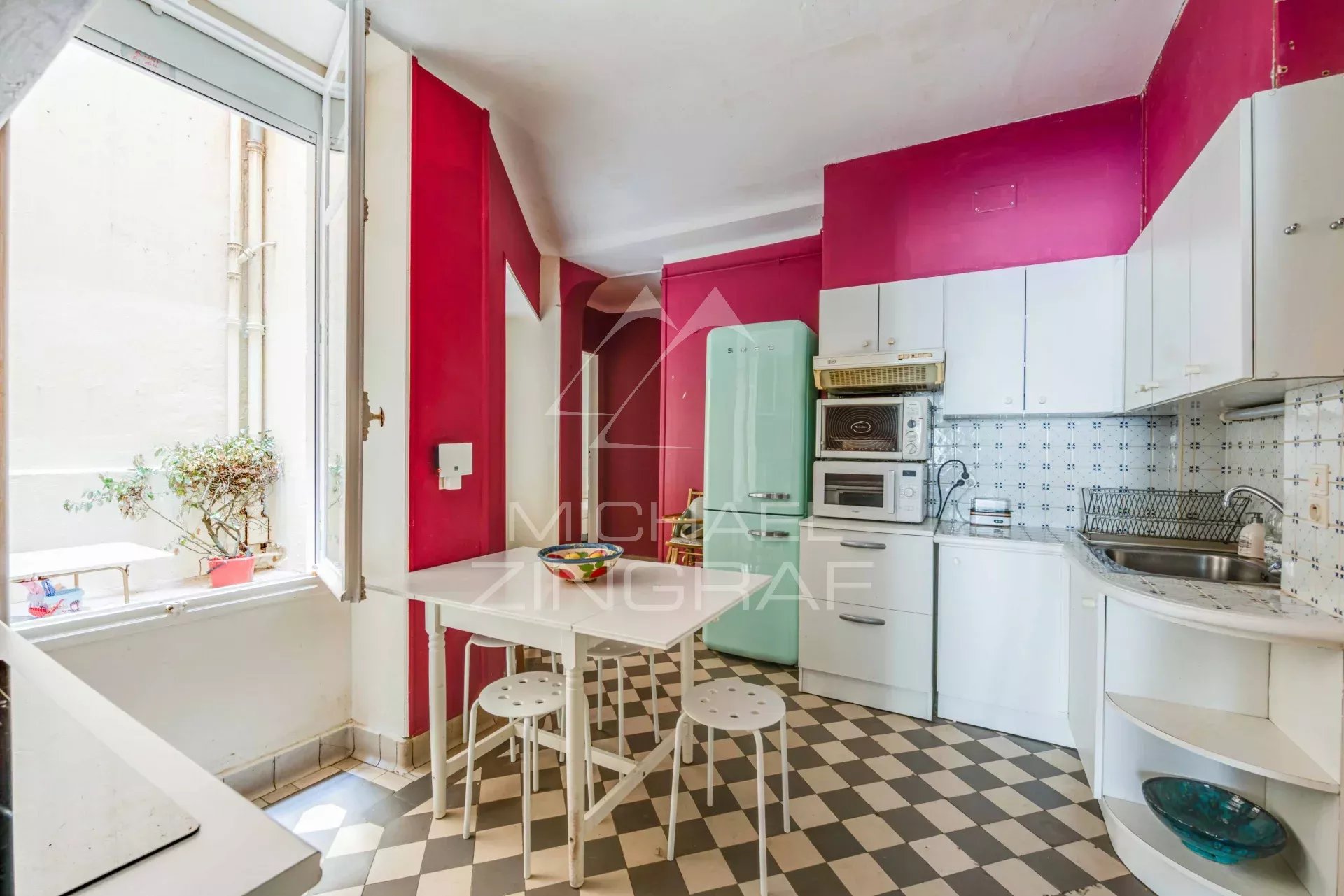 Cuisine moderne avec murs roses et carrelage noir et blanc dans un appartement à Biarritz.
