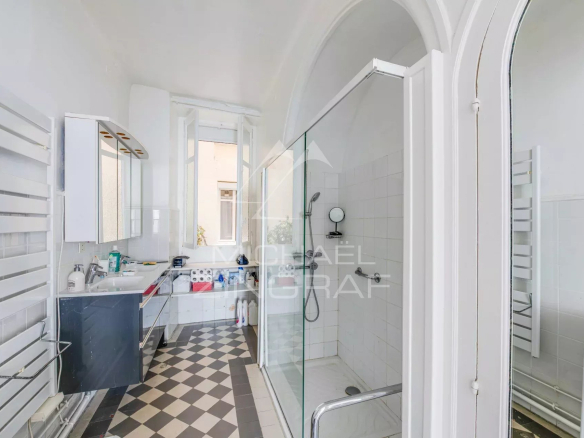 Salle de bain moderne avec douche et lavabo, carrelage noir et blanc, fenêtre laissant entrer la lumière.