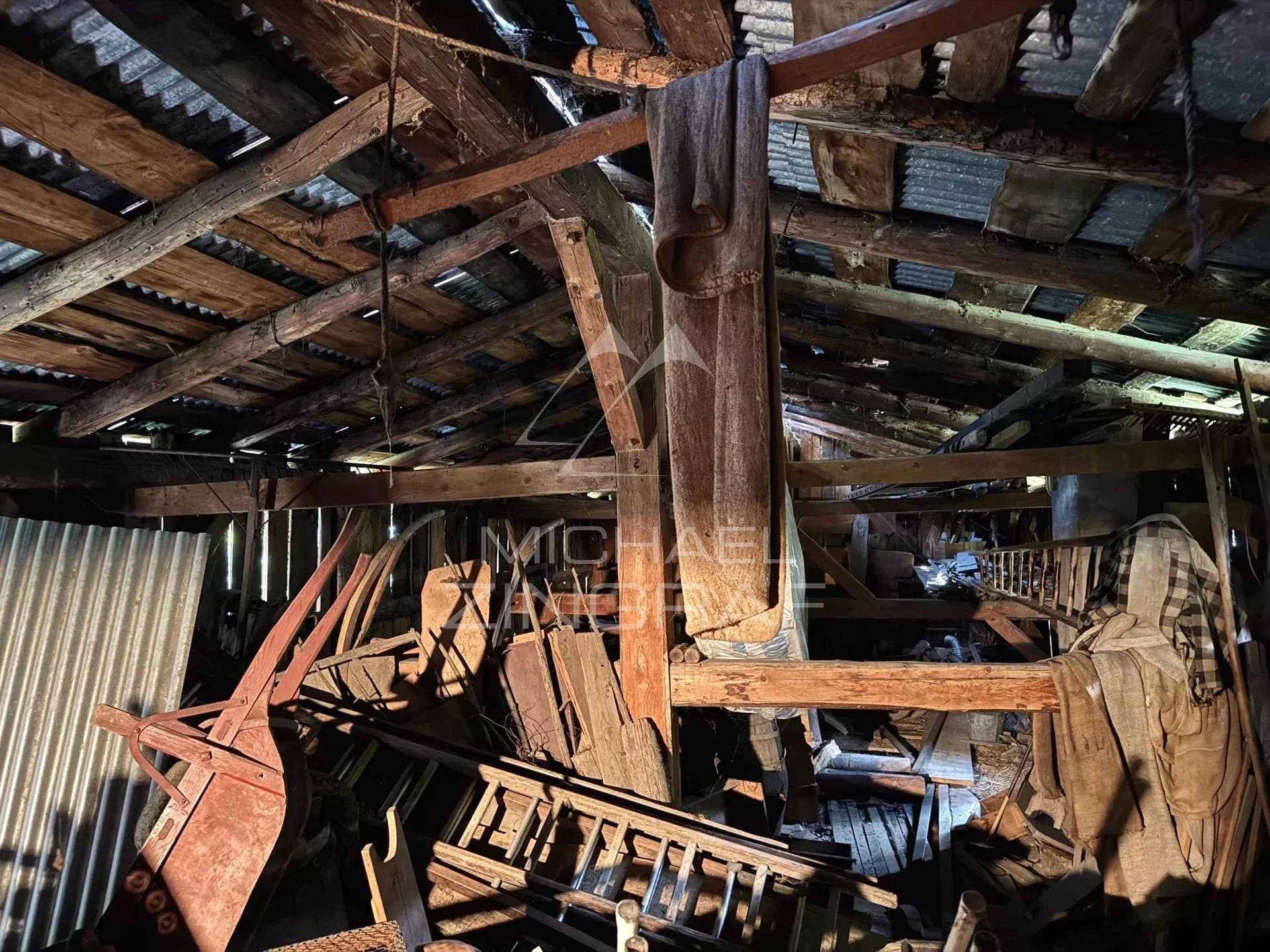 Intérieur d'une ferme ancienne à rénover avec des poutres en bois et des objets de ferme