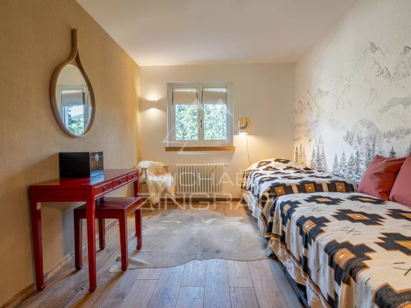 Chambre d'un appartement rénové à Megève avec deux lits et un bureau rouge.