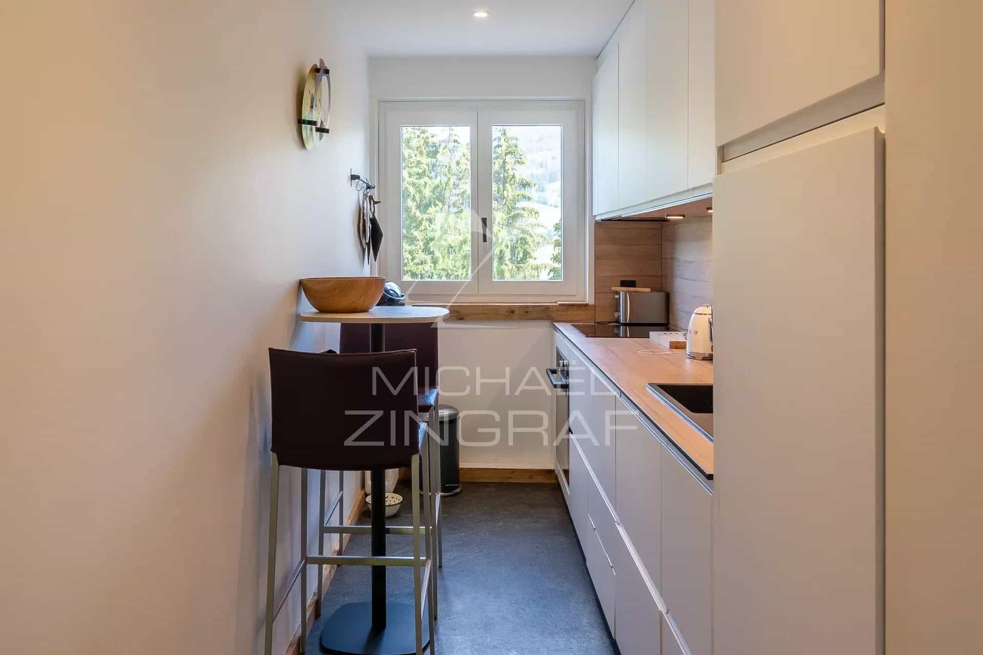 Cuisine moderne et lumineuse d'un appartement rénové à Megève, avec bar et fenêtres.