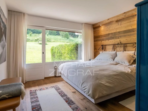 Chambre d'un appartement rénové avec vue sur la nature à Megève, murs en bois et lit confortable.