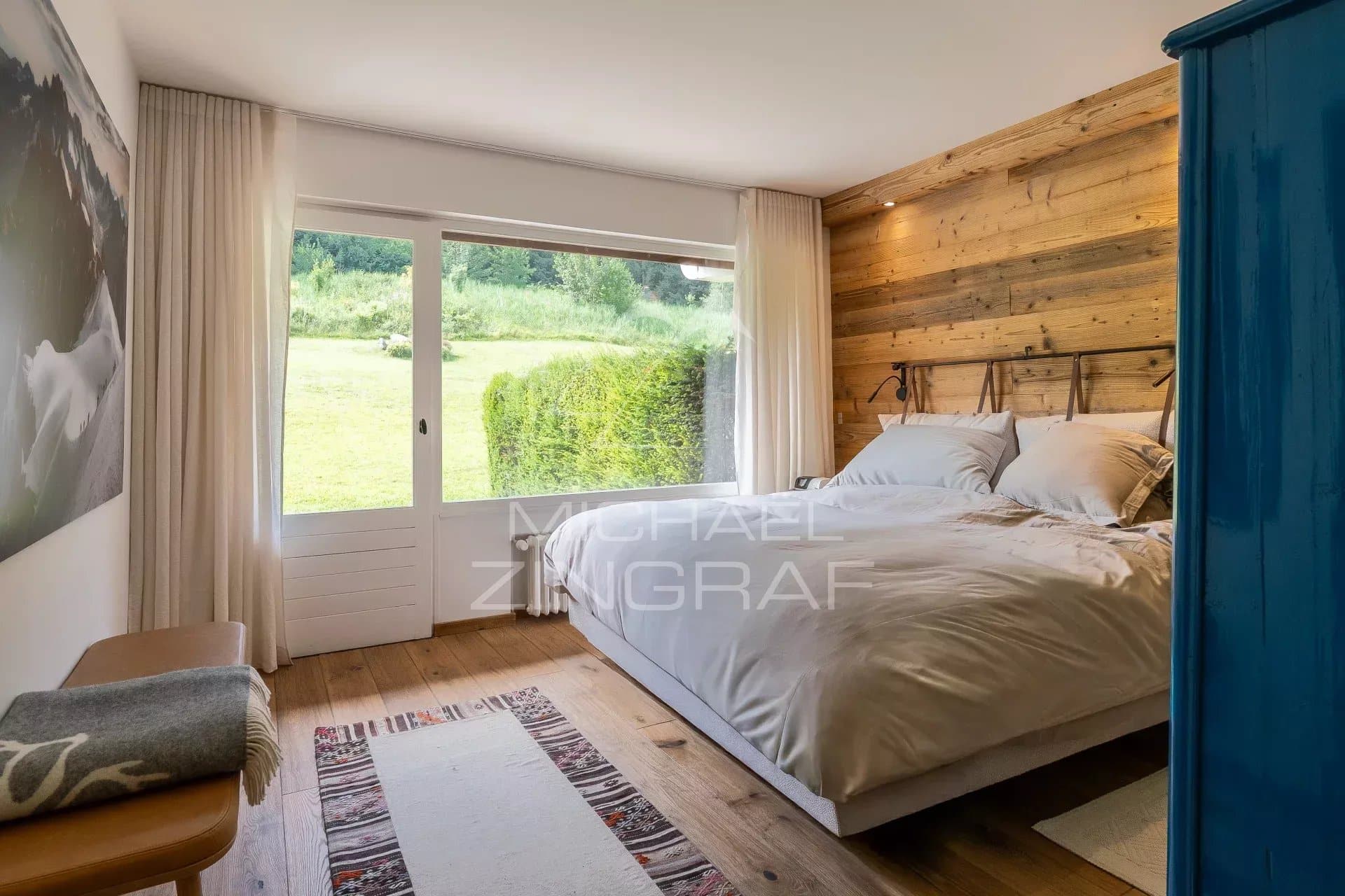 Chambre d'un appartement rénové avec vue sur la nature à Megève, murs en bois et lit confortable.